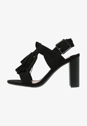 Czarne zamszowe sandały na wysokim obcasie z detalem w postaci frędzli, otwartym palcem, regulowanym paskiem wokół kostki i teksturowanym słupkowym obcasem.
