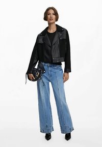 Veste en cuir noire courte, jean bleu clair ample, bottes noires à talons hauts, et un petit sac à main noir avec des détails texturés.