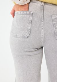 Jeans grigi in denim con un design aderente e due tasche posteriori. Il tessuto ha una texture liscia con una leggera elasticità.