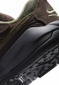 Brązowo-oliwkowy sneaker z teksturowaną zamszową i oddychającą siateczkową cholewką, wyposażony w czarną gumową podeszwę z wzorzystym bieżnikiem.