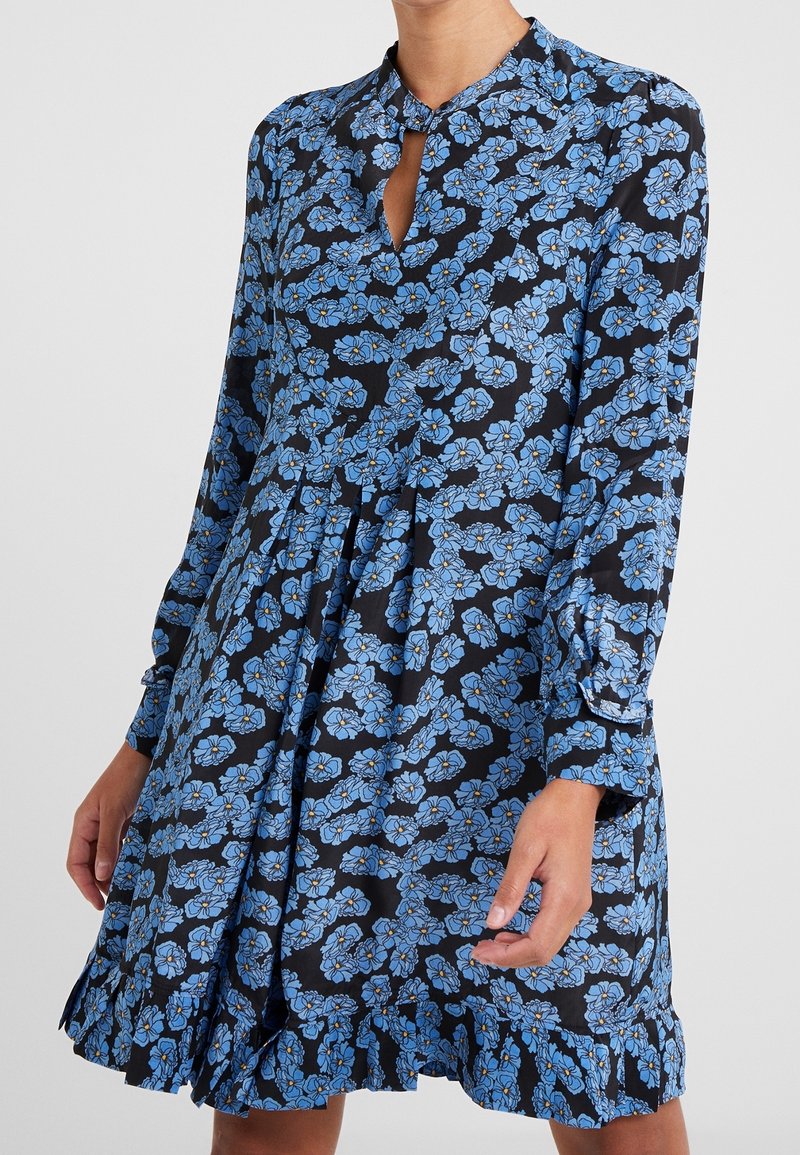 Kukkamekko, jossa tummansininen pohja ja sinisiä kukkakuvioita, pitkät hihat, napillinen kaulus ja röyhelöhelma. Valmistettu kevyestä kankaasta.