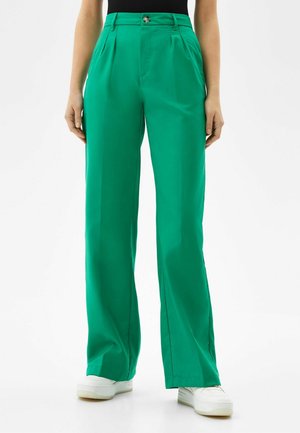 Pantalons larges verts en tissu lisse, dotés d'une taille haute, de plis à l'avant et d'une fermeture à un bouton en métal.