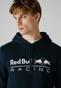 Marineblauwe hoodie van een katoenmix, met het witte logo "Red Bull Racing" en een afbeelding van twee stieren, voorzien van een trekkoord bij de capuchon.