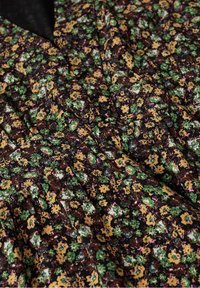 Tissu foncé avec un motif floral dense et petit dans des nuances de jaune, vert et violet, montrant des détails de couture froncée et plissée.
