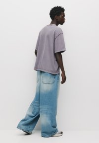 Overdimensional grå bomulds t-shirt parret med vide, falmede blå denim jeans, der har lommer og en let gradient effekt på stoffet.
