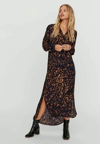 Lang, svart kjole med leopardmønster i ravfarger. Har v-hals, lange ermer og sideslitt. Glatt stoff med flytende design.