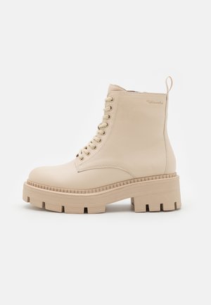 Beige snørestøvle til anklen med tyk rillede sål og trækflig ved hælen, lavet af glat læderlignende materiale.