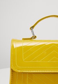 Borsa a tracolla in pelle verniciata gialla brillante con un motivo a zigzag trapuntato, forma strutturata e manico corto con accessori in metallo argentato.