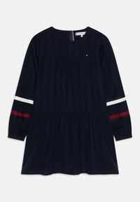 Marineblaues Kleid mit langen Ärmeln, gerafftem Oberteil und ausgestelltem Saum. Mit roten und weißen Streifen an den Ärmeln und einem kleinen Logo auf der Brust.