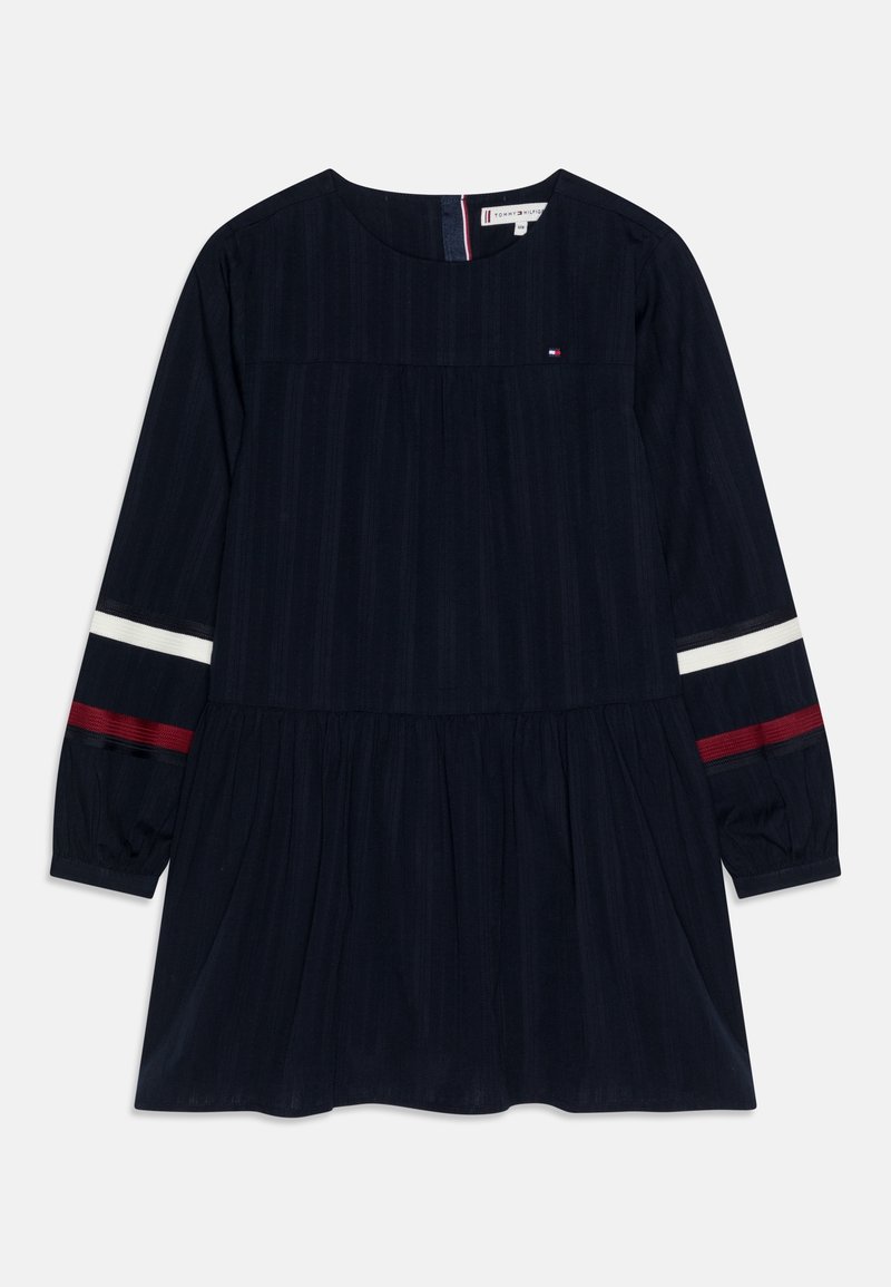 Marineblaues Kleid mit langen Ärmeln, gerafftem Oberteil und ausgestelltem Saum. Mit roten und weißen Streifen an den Ärmeln und einem kleinen Logo auf der Brust.