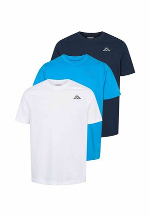 Nuori mies, jolla on lyhyet hiukset, valkoinen logollinen t-paita ja tummanvihreät cargohousut, seisoo käsi taskussa.