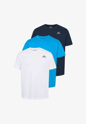 Rövid hajú fiatal férfi fehér logós pólóban és sötétzöld cargo nadrágban, az egyik kezét zsebre téve áll.