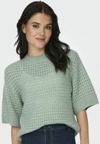 Maglione in maglia verde menta chiaro con un motivo a punto aperto, maniche corte e colletto a coste. Il tessuto testurizzato aggiunge interesse visivo.