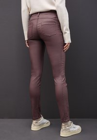 Jeans slim fit en color malva con un brillo sutil, dos bolsillos traseros y una textura suave, combinados con zapatillas blancas con acentos beige.
