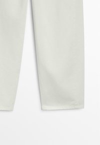 Partie inférieure d’un pantalon beige clair à jambes droites avec couture visible à l’ourlet sur fond blanc.