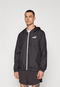 Chaqueta rompevientos negra con cremallera frontal, capucha ajustable, puños elásticos y un logo blanco de PUMA en el pecho. Material suave y ligero.