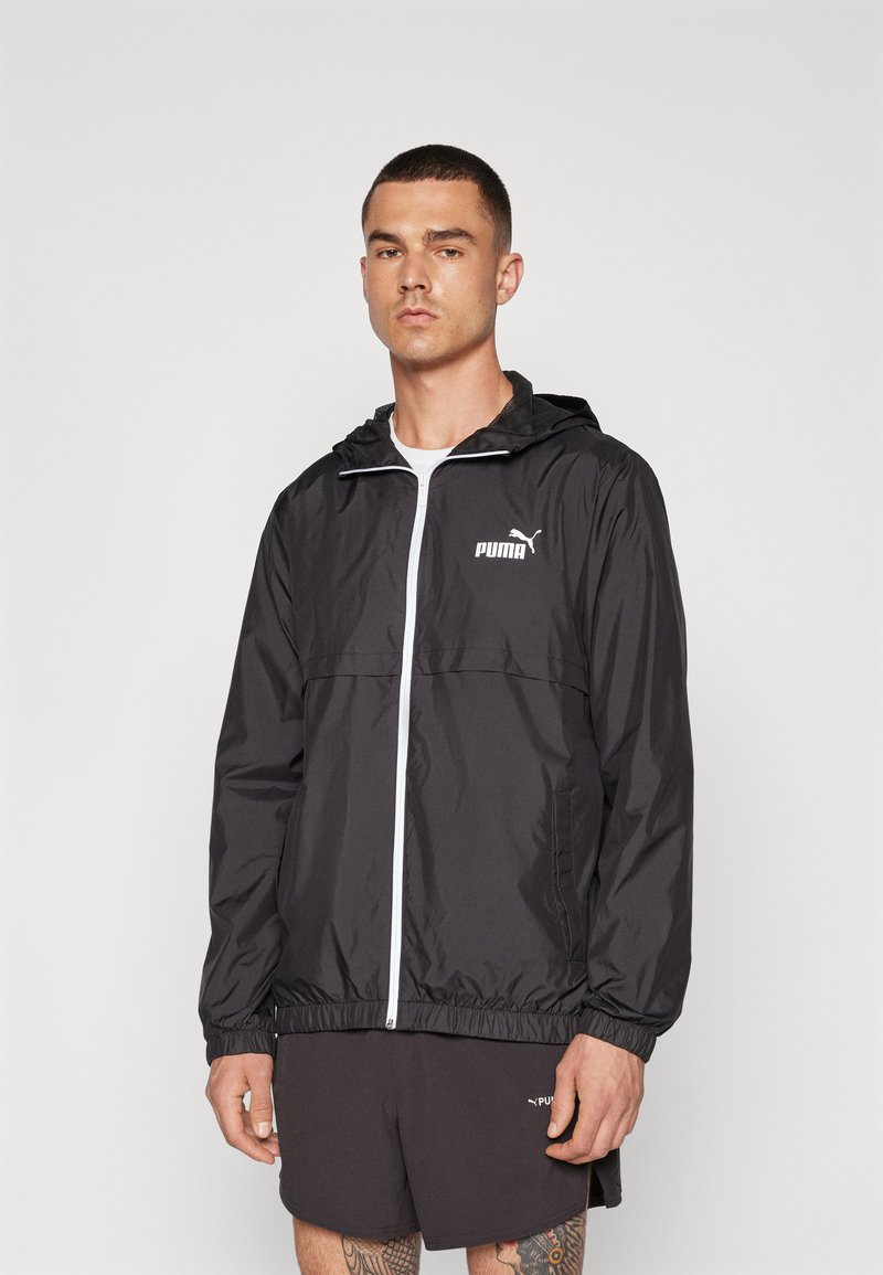 Chaqueta rompevientos negra con cremallera frontal, capucha ajustable, puños elásticos y un logo blanco de PUMA en el pecho. Material suave y ligero.