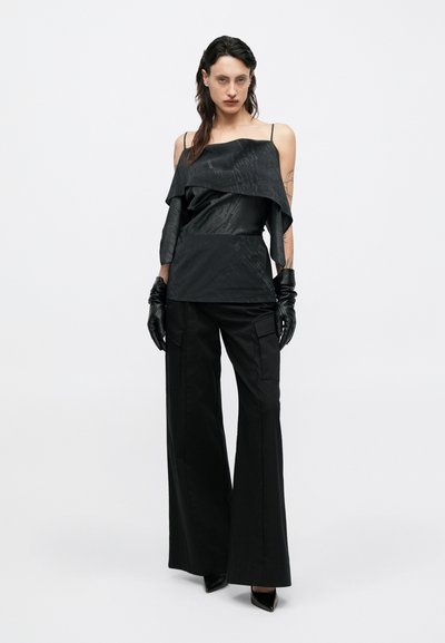 Top nero senza maniche con design a strati e texture sottile, abbinato a pantaloni neri a gamba larga. Il modello indossa guanti neri e tacchi.