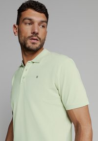 Lichtgroen poloshirt van katoen, met een klassieke kraag, twee knopen bij de sluiting en een subtiel logo op de borst. Korte mouwen.