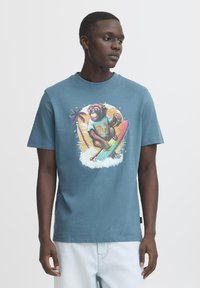 Blå bomulds T-shirt med et farverigt monkey grafik på et surfbræt, omgivet af palmetræer og bølger. Korte ærmer og rund halsudskæring.