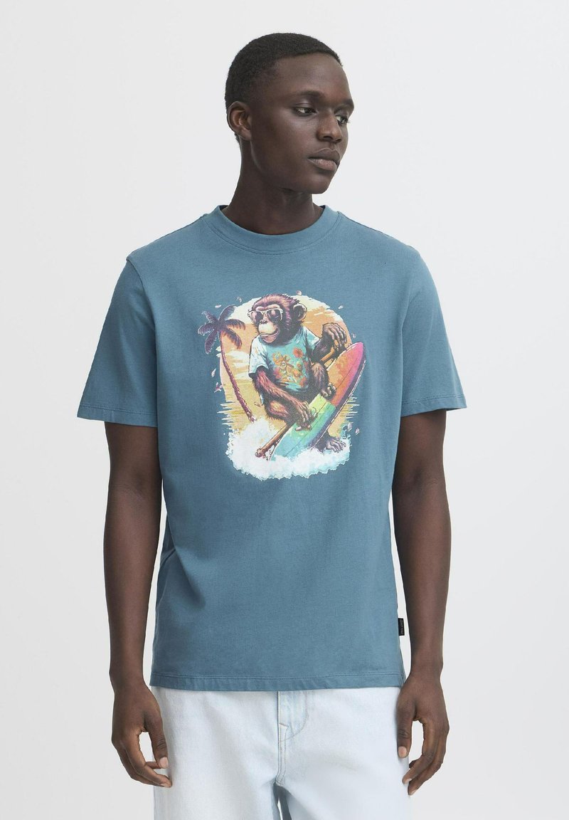 Blå bomulds T-shirt med et farverigt monkey grafik på et surfbræt, omgivet af palmetræer og bølger. Korte ærmer og rund halsudskæring.