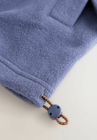 Light blue fleece material with soft texture. Features a stitched hem, a brown drawstring with a blue plastic toggle.