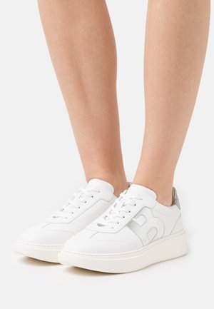 Sneakers bianchi in pelle con un tallone grigio testurizzato, suola piatta e dettagli loghi laterali in una sottile cucitura grigia chiara.