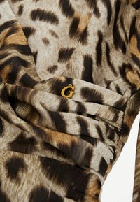 Leopardo rašto audinys su rudos, juodos ir smėlinės spalvos tonais, su aukso „G“ logotipo akcentu raukinyje.