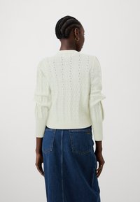 Lys grønn strikket genser med et teksturert sikksakkmønster og ballongsleeves, kombinert med en mørkeblå denimskjørt med baklommer.