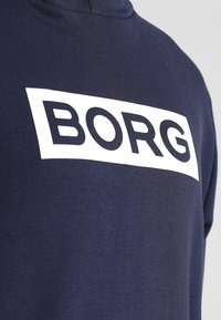 Sudadera de color azul marino con un tejido texturizado, que presenta un gran gráfico rectangular blanco con el texto "BORG" en letras negras en negrita.