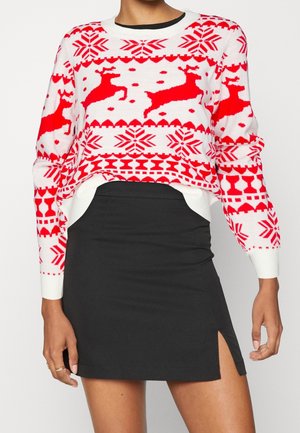 Pull de Noël blanc et rouge avec motifs de rennes et flocons de neige, accompagné d'une mini-jupe noire avec une petite fente latérale.