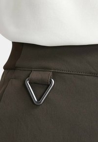 Brun tygmidja med en triangulär svart metalldetalj. Slät yta med synlig sömnad längs sidan.