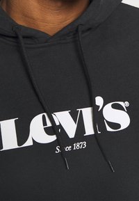 Sweat à capuche noir avec un logo blanc "Levi's" et le texte "Depuis 1873". Comprend des cordons de serrage et un tissu texturé.