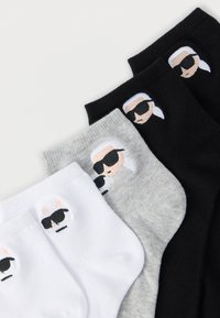 Three pairs of crew socks in white, gray, and black featuring embroidered cartoon faces with sunglasses. Textured fabric, ribbed cuffs.
