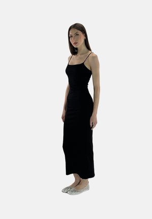 Schwarzes, figurbetontes, ärmelloses Kleid mit dünnen Trägern; glatte Textur; knielang; kombiniert mit silbernen, verzierten Ballerinas.