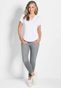 Witte v-hals t-shirt, grijze slim-fit jeans en witte sneakers. De outfit heeft een casual pasvorm met een gladde, zachte textuur en een eenvoudig ontwerp.
