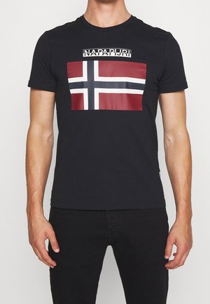 Man wearing black t-shirt with red, white, and blue Nordic cross flag and "NAPAPIJRI" text above the flag on chest.