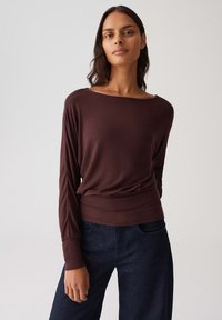 Braunes Langarmoberteil mit weitem Ausschnitt, weichem Material, lockerer Passform und geripptem Saum, kombiniert mit dunkelblauen weiten Jeans.
