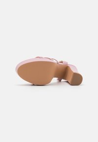 Rosa klacksandal med en slät syntetisk ovandela, tunna remmar, rund tå och en strukturerad beige gummisula. Spänne som accent på remmen.
