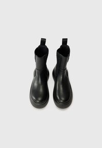 Bottines noires en cuir lisse, dotées de panneaux élastiques sur les côtés, de semelles en caoutchouc texturé et d'une languette à l'arrière pour un enfilage facile.