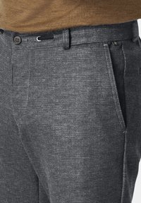 Grau karierte Hose mit feiner Textur, ausgestattet mit einem einzelnen Knopfverschluss und seitlichen Taschen. Der Stoff hat ein feines, wollartiges Aussehen.