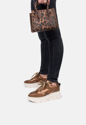 Zapatillas metálicas bronce con suelas gruesas blancas, combinadas con un pequeño bolso marrón de estampado leopardo. Unos jeans skinny negros complementan el conjunto.
