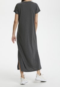 Osoba w ciemnoszarej, krótkosleeve maksij sukience z bocznym rozcięciem i białych trampkach Adidas, stojąca plecami do kamery.