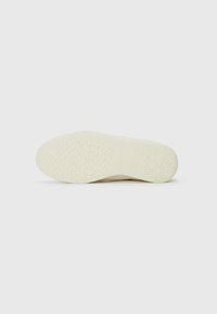Semelle de chaussure couleur crème avec un motif texturé composé de petits hexagones et étoiles en relief pour l'adhérence, présentée sur un fond blanc.