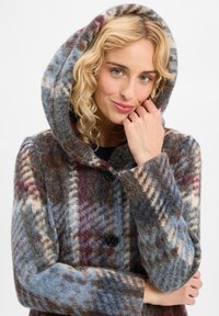 Wollmantel mit Kapuze, der ein kariertes Muster in Blau, Braun und sanften Creme-Tönen aufweist. Schwarze Knöpfe und eine strukturierte Oberfläche.