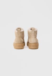 Botas de tornozelo em camurça bege com forro em shearling, sola de borracha resistente e laço na parte de trás; branding mínimo na sola.