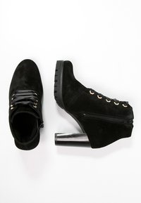 Bottes ankle en suede noir avec un bout rond, un laçage à l'avant et une fermeture éclair sur le côté. Elles présentent un talon metallic épais et des œillets décoratifs.