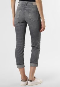 Jeans en denim gris, coupe courte avec revers roulés, présentant une coupe ajustée et deux poches arrière. Portés avec des baskets à talon orné d'un motif.
