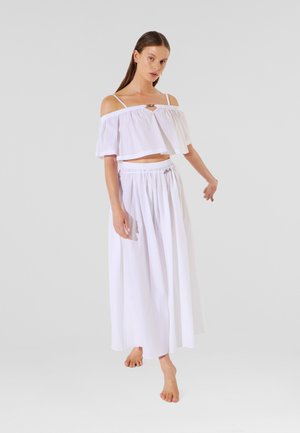 Witte off-shoulder crop top met een ruchesontwerp, gecombineerd met een lange, vloeiende witte rok met een elastische tailleband.