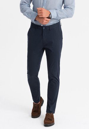 Navy blue cotton chinos with a slim fit, featuring a flat front and side pockets. Worn with a striped shirt and brown suede shoes.